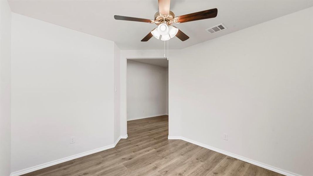 Interior room featuring wood-finish flooring, light-toned walls, a bronze-finish ceiling fan with integrated lighting, and white baseboards Interior room featuring wood-finish flooring, light-toned walls, a bronze-finish ceiling fan with integrated lighting, and white baseboards