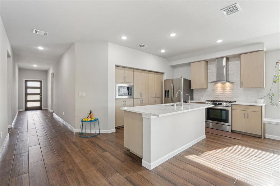 Kitchen featuring an island with sink, stainless steel appliances, hardwood / wood-style flooring, and wall chimney range hood