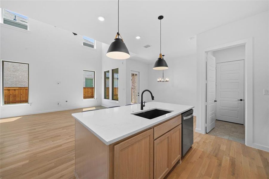 Kitchen island featuring a white countertop, undermount sink with a matte black faucet, and pendant lighting