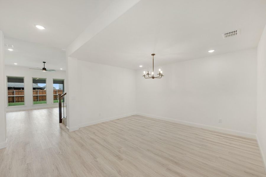 Open living and dining area with light wood floors, chandelier, ceiling fan, and backyard windows