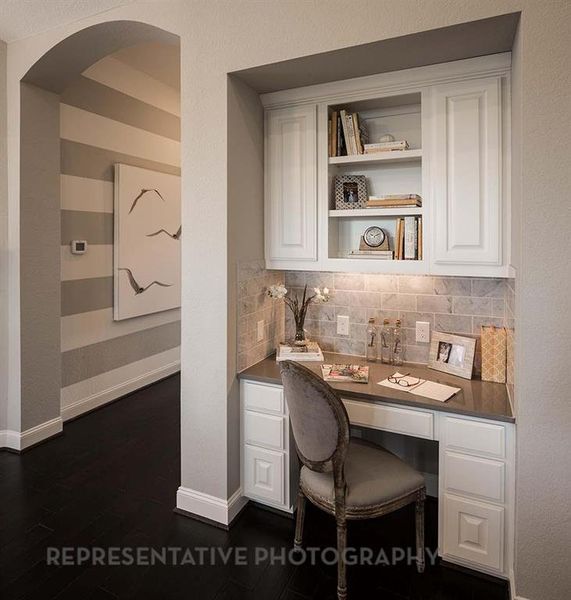 Office space with built in study area, dark wood finished floors, a textured wall, and arched walkways Office space with built in study area, dark wood finished floors, a textured wall, and arched walkways