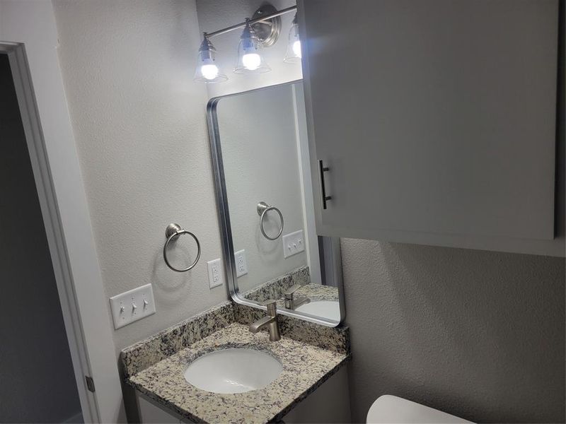 Bathroom vanity featuring a speckled countertop, undermount sink, and brushed nickel faucet