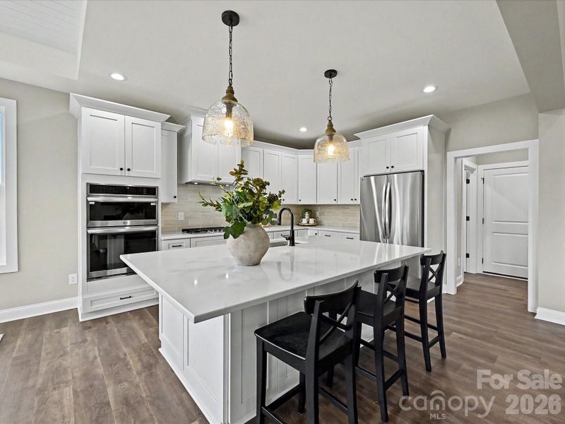 Designer kitchen features a massive quartz island, custom cabinetry, stainless steel appliances, and an open layout perfect for everyday living and entertaining.