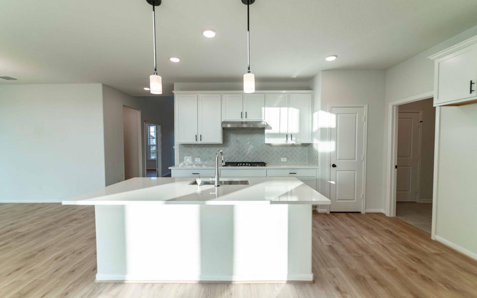 Kitchen featuring tasteful backsplash, an island with sink, white cabinets, light wood-style floors, and hanging light fixtures