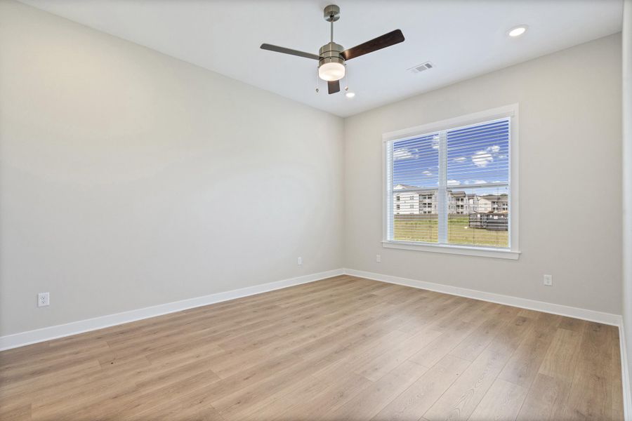 Spacious room featuring wood-finish flooring, neutral wall paint, and a large window with white blinds Spacious room featuring wood-finish flooring, neutral wall paint, and a large window with white blinds
