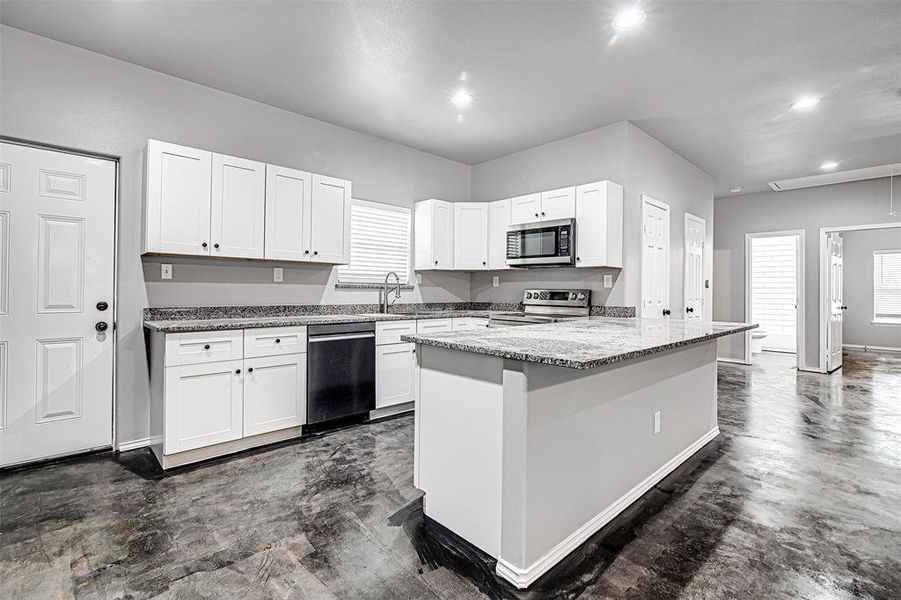 Kitchen featuring a kitchen island, white cabinetry, appliances with stainless steel finishes, light stone counters, and sink