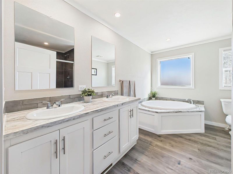 Primary Bathroom – A spa-like retreat with dual vanities, a soaking tub beneath a large frosted window, and a walk-in shower, all accented by modern finishes and neutral tones.
