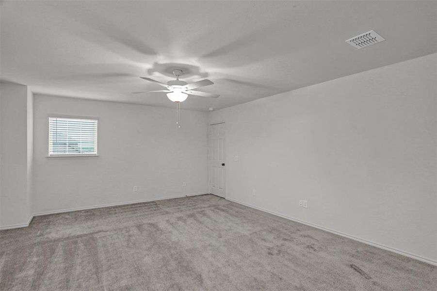 Spacious room featuring neutral carpet, white walls, a white ceiling fan with integrated lighting, a rectangular window with white blinds, and a white door with a black handle