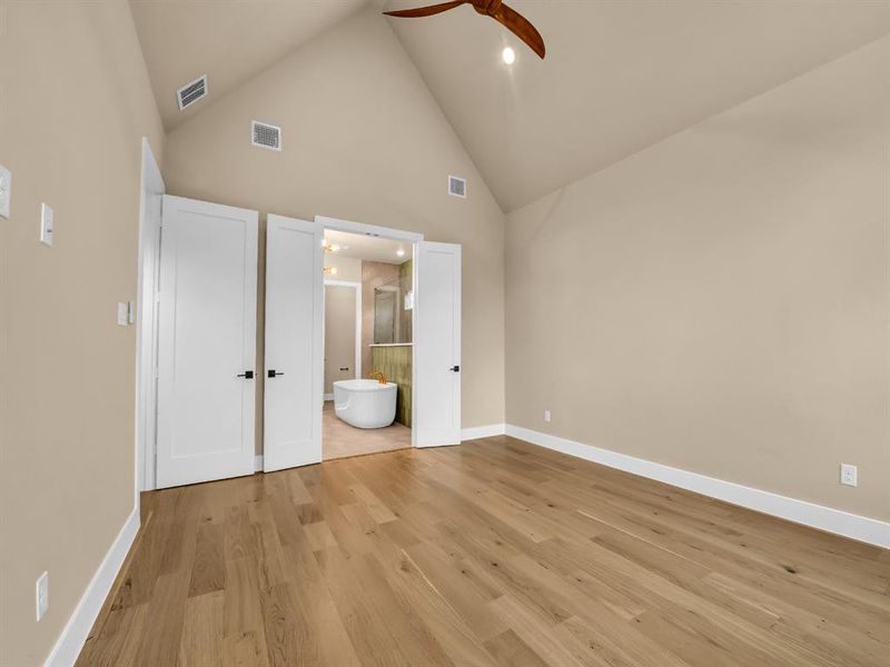 Unfurnished bedroom featuring light wood-type flooring, high vaulted ceiling, ensuite bath, and ceiling fan