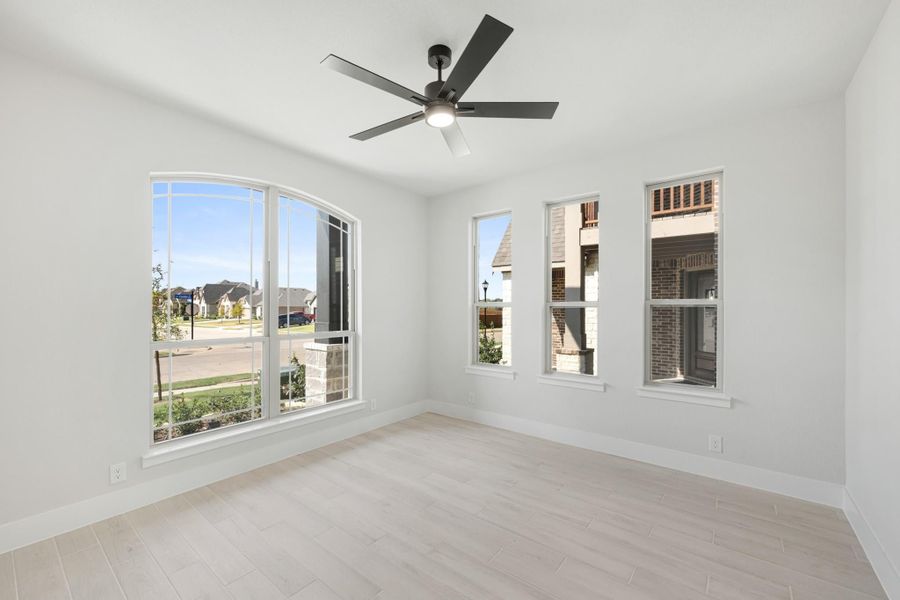 Empty room with light wood floors, ceiling fan, and large arched windows overlooking a neighborhood street