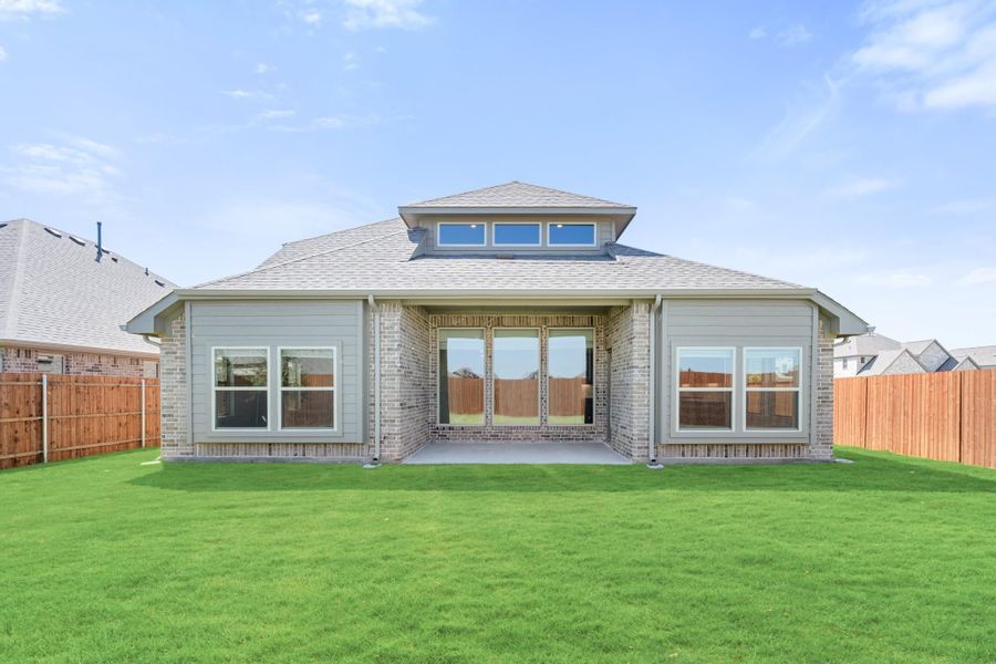 Rear exterior of single-story brick home with covered patio, large windows, and fenced backyard lawn Rear exterior of single-story brick home with covered patio, large windows, and fenced backyard lawn