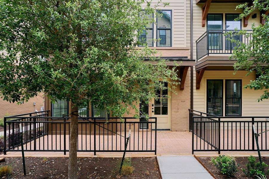Exterior facade featuring light-colored siding, brick accents, a ground-level patio with black metal railings, a balcony with matching railings, and mature trees Exterior facade featuring light-colored siding, brick accents, a ground-level patio with black metal railings, a balcony with matching railings, and mature trees