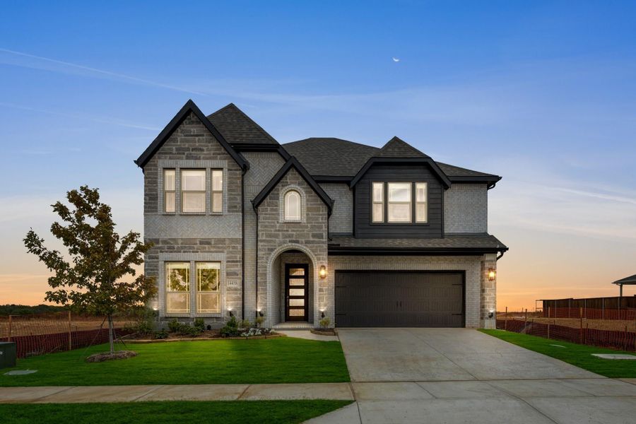 Two-story brick and stone home with arched entry, two-car garage, and green front lawn at dusk