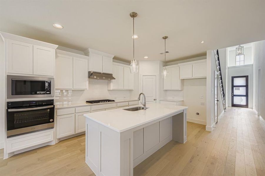 Kitchen featuring stainless steel appliances, light wood-style floors, decorative backsplash, white cabinetry, and recessed lighting Kitchen featuring stainless steel appliances, light wood-style floors, decorative backsplash, white cabinetry, and recessed lighting