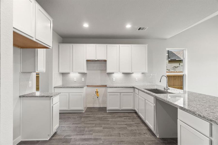 Culinary haven, featuring granite countertops, a tile backsplash, stainless steel appliances (to be installed), and 42” upper cabinets. Sample photo, actual color and selections may vary.