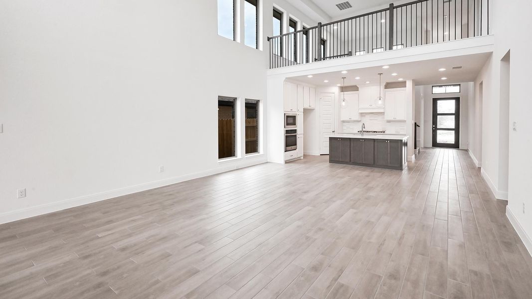 Unfurnished living room featuring a sink, light wood-style flooring, baseboards, and a towering ceiling