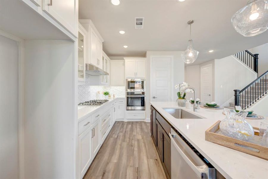 Two tone kitchen featuring dual tone cabinets, stainless steel appliances, light wood-style flooring, hanging light fixtures, and glass insert cabinets