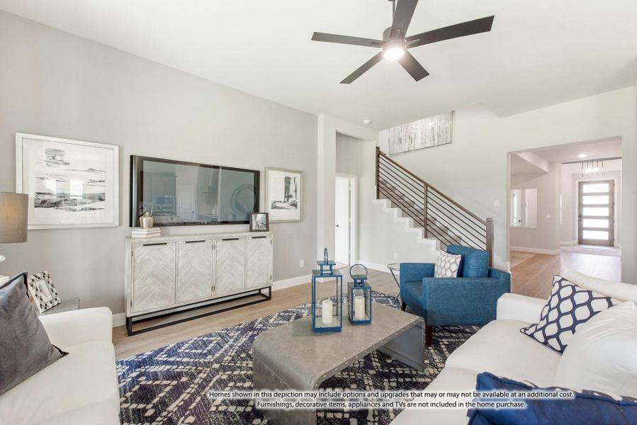 Living room with white sofa, blue accent chairs, ceiling fan, and staircase with metal railing Living room with white sofa, blue accent chairs, ceiling fan, and staircase with metal railing