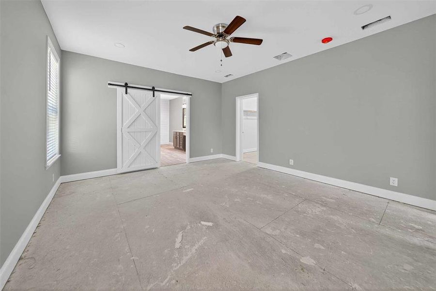 Unfurnished bedroom featuring a barn door, a ceiling fan, and a spacious closet