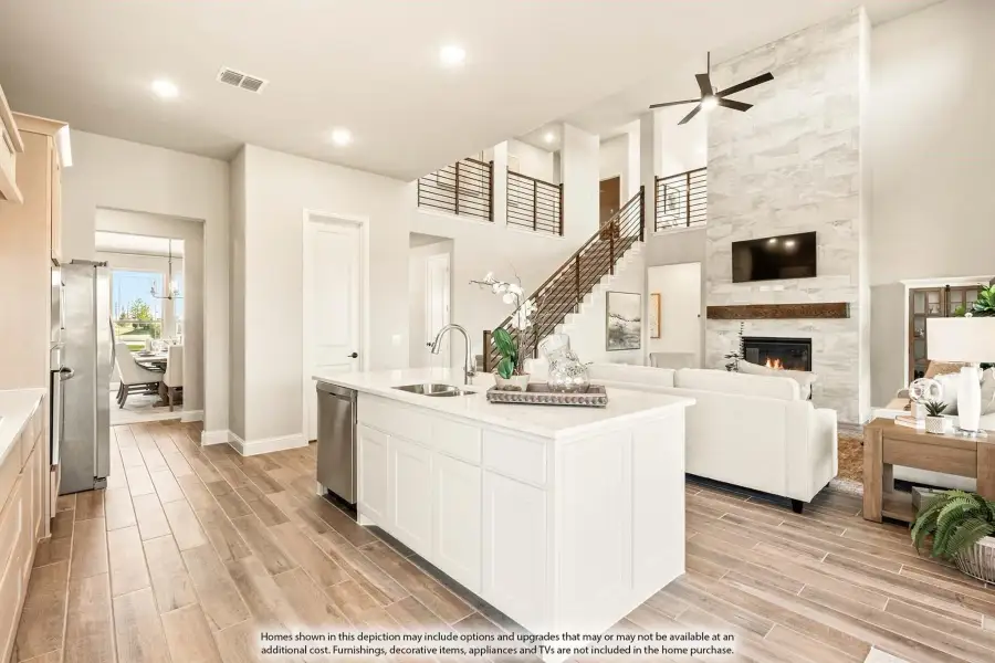 Open-concept kitchen with white island and sink, flowing into living room with stone fireplace and two-story ceiling