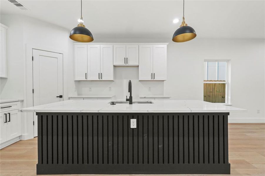 Kitchen with white cabinets, light wood finished floors, light stone counters, and a center island with sink Kitchen with white cabinets, light wood finished floors, light stone counters, and a center island with sink