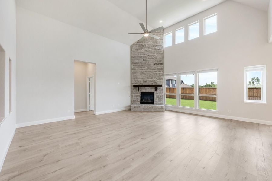 Open living room with vaulted ceiling, stone fireplace, ceiling fan, and light hardwood floors
