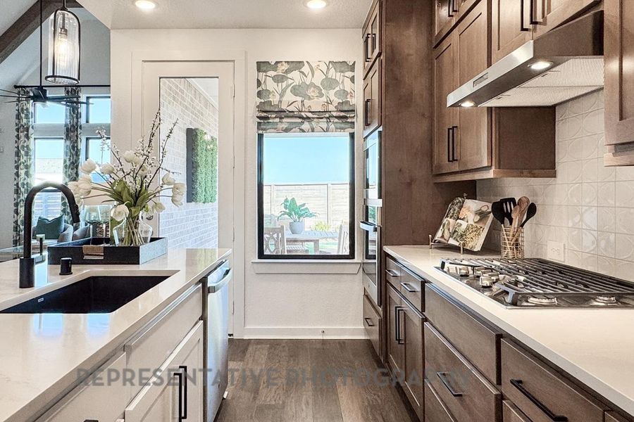 Kitchen featuring stainless steel appliances, under cabinet range hood, dark wood-style floors, light countertops, and tasteful backsplash