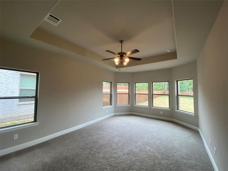 Master bedroom retreat offers tray ceing, large bay window, and ceiling fan