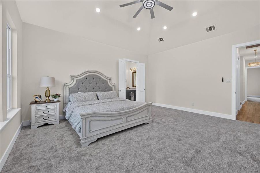 Spacious room featuring vaulted ceilings, recessed lighting, a ceiling fan, light gray carpeting, and a large window Spacious room featuring vaulted ceilings, recessed lighting, a ceiling fan, light gray carpeting, and a large window