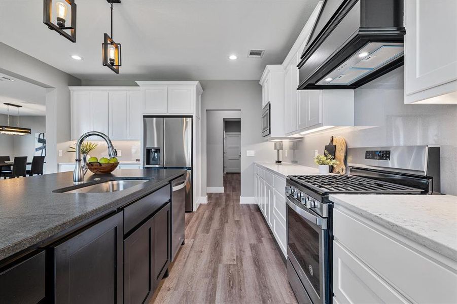 Kitchen with light hardwood / wood-style flooring, white cabinetry, appliances with stainless steel finishes, sink, and decorative light fixtures