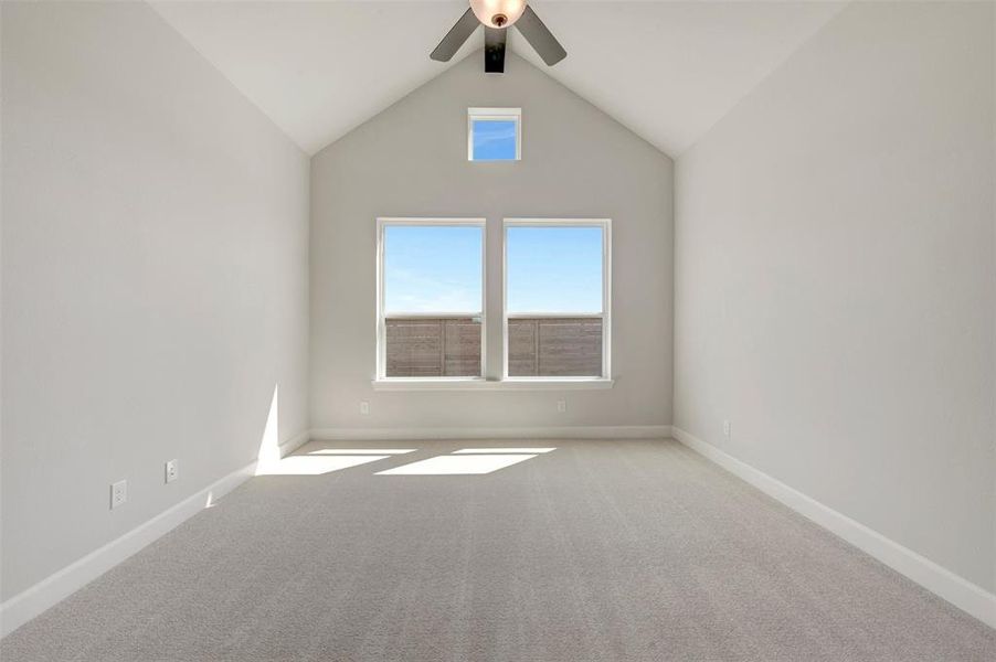 Vaulted ceiling room featuring three windows, neutral wall paint, light gray carpeting, and a ceiling fan with light fixture