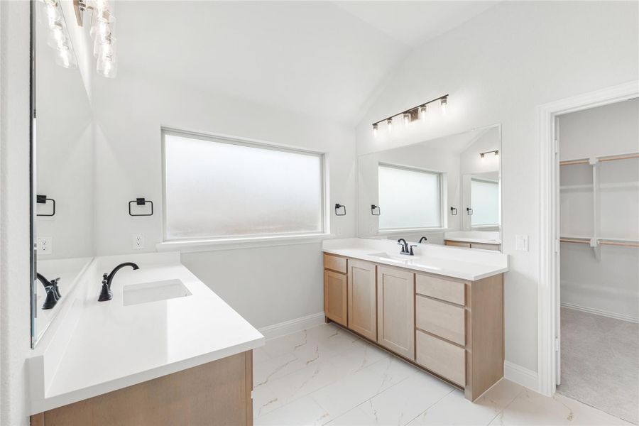 Master bathroom with dual vanities, white countertops, marble tile floors, and walk-in closet access Master bathroom with dual vanities, white countertops, marble tile floors, and walk-in closet access