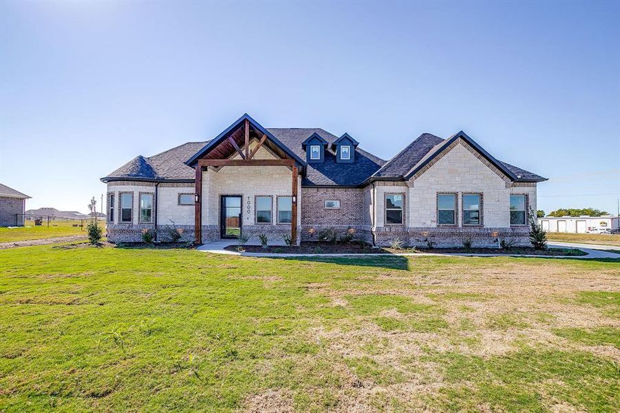 View of front facade featuring a front lawn, stone siding, brick siding, and roof with shingles
