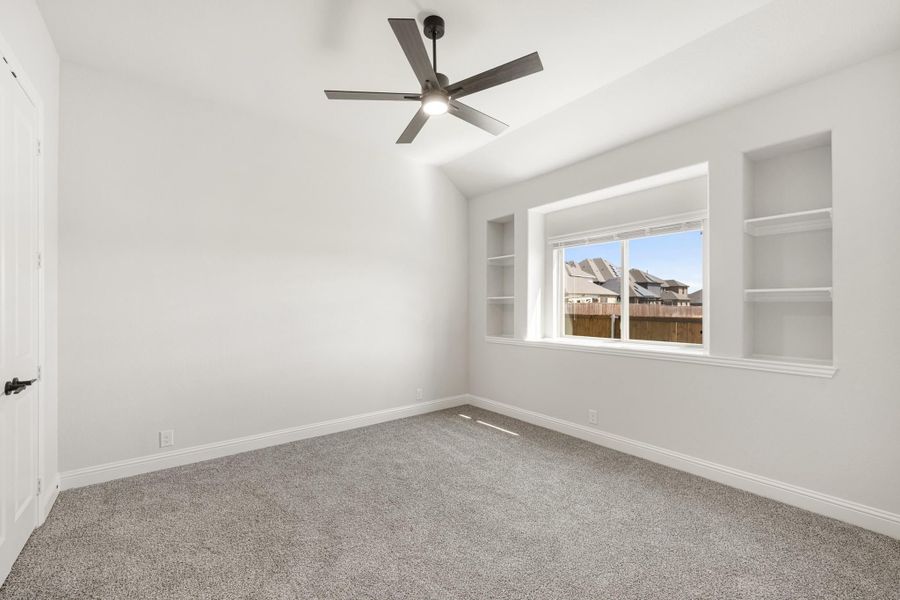Empty bedroom with vaulted ceiling, ceiling fan, built-in shelves, and carpet flooring Empty bedroom with vaulted ceiling, ceiling fan, built-in shelves, and carpet flooring