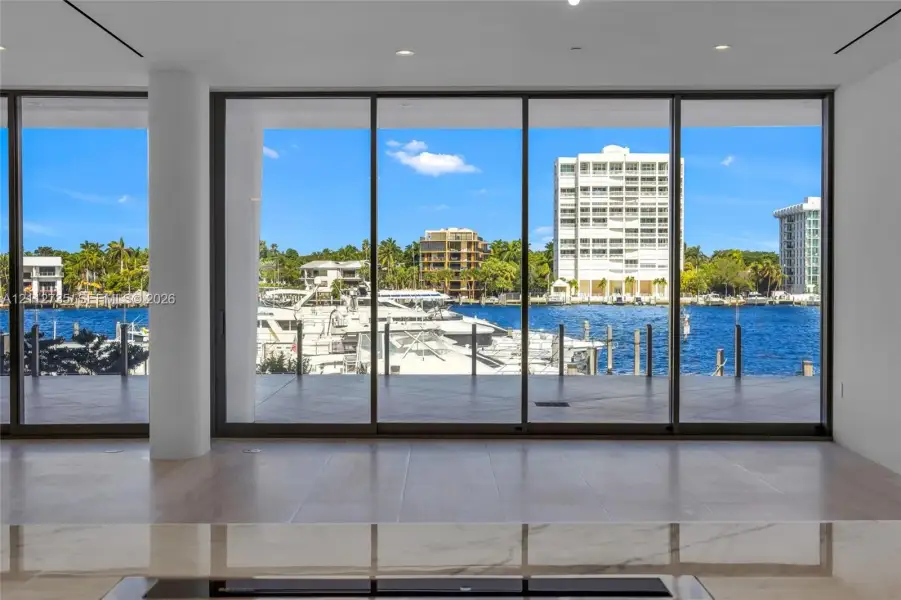 Floor-to-ceiling glass sliding doors, expansive waterfront exposure, polished stone countertop, and light-toned tile flooring