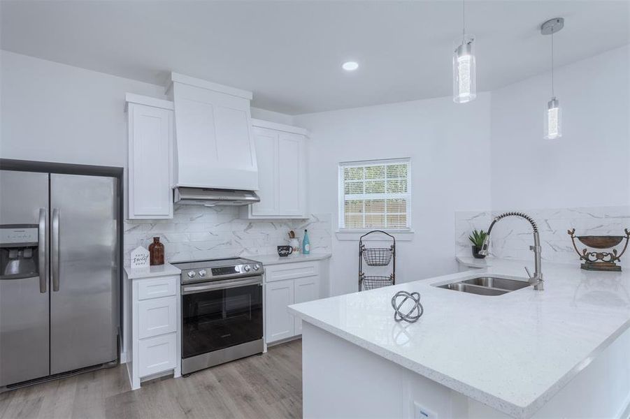 Kitchen with sink, white cabinetry, kitchen peninsula, custom exhaust hood, and appliances with stainless steel finishes