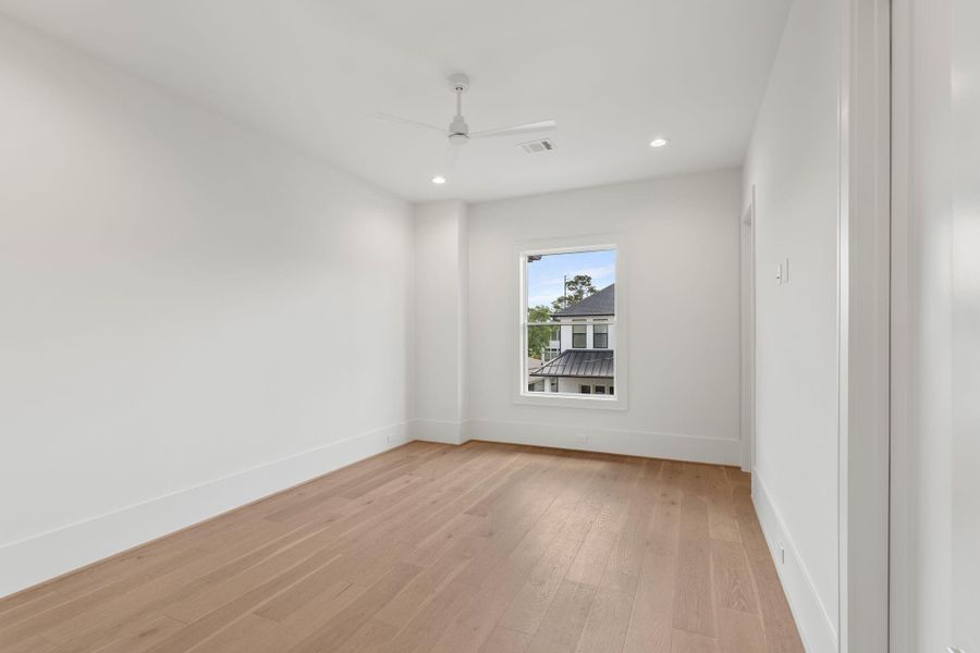 A bright and spacious secondary bedroom features wide-plank flooring, large windows, and a neutral palette that allows for versatile use.