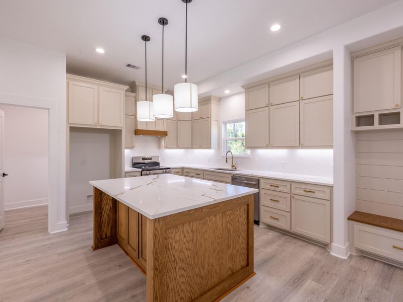 This modern kitchen features a spacious layout with light-colored cabinetry and a large island with a marble countertop. It includes stainless steel appliances, ample storage, and elegant pendant lighting, creating a bright and inviting space.
