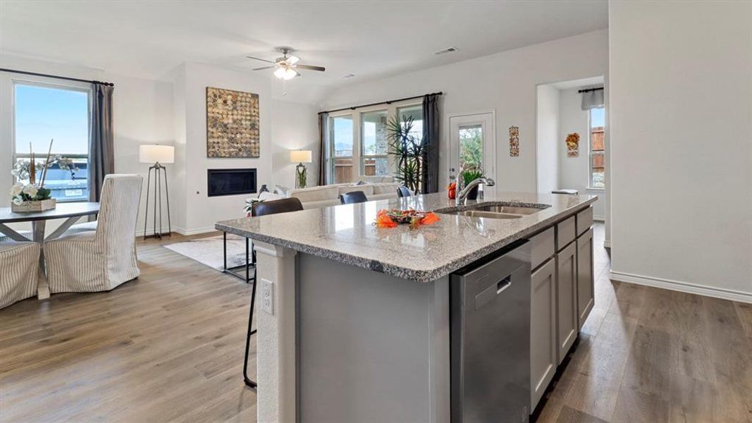 Kitchen with light stone countertops, dishwasher, dark wood-type flooring, a center island with sink, and a glass covered fireplace