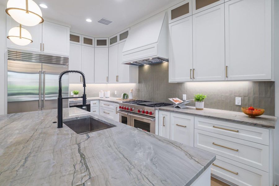 Spacious kitchen featuring a large island with an undermount sink and matte black pull-down faucet, white shaker cabinetry with brass hardware, stainless steel appliances, and a tiled backsplash