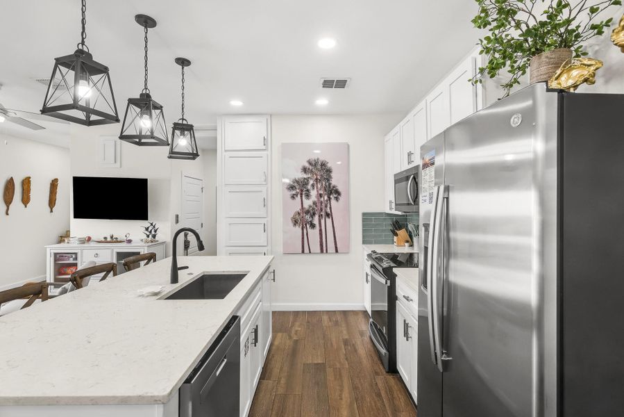 Kitchen with appliances with stainless steel finishes, white cabinets, dark wood finished floors, hanging light fixtures, and a kitchen island with sink Kitchen with appliances with stainless steel finishes, white cabinets, dark wood finished floors, hanging light fixtures, and a kitchen island with sink