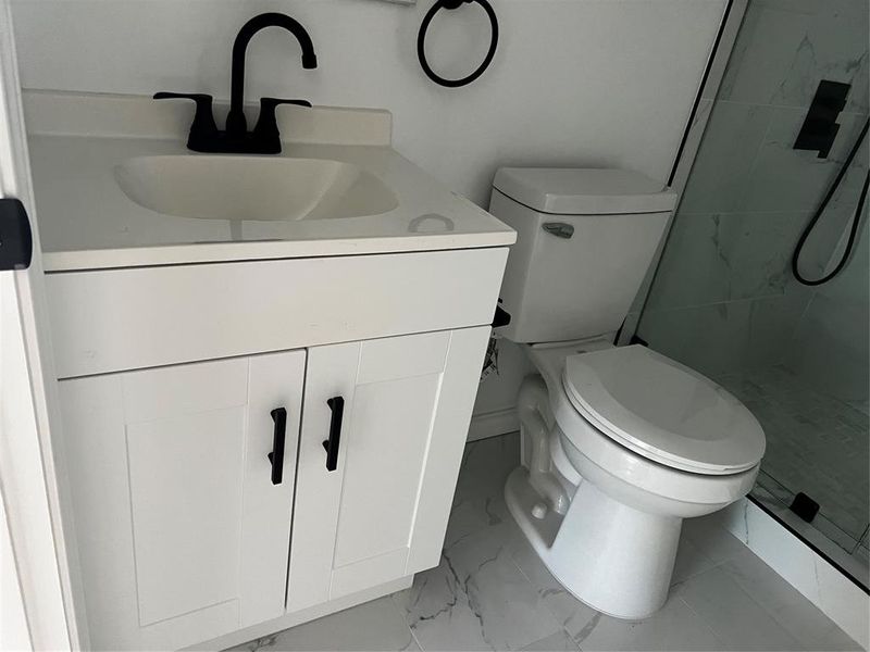 Bathroom with tiled shower, tile patterned floors, vanity, and toilet