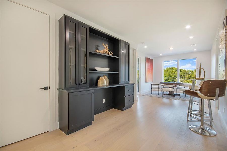 Bar featuring open shelves, glass insert cabinets, light wood-style floors, recessed lighting, and dark cabinets Bar featuring open shelves, glass insert cabinets, light wood-style floors, recessed lighting, and dark cabinets
