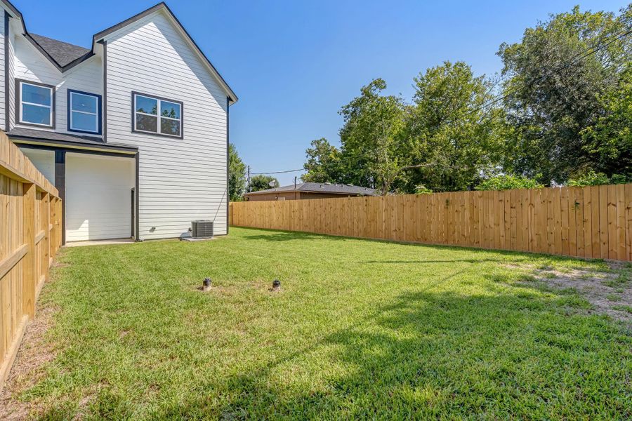 Backyard view featuring a covered patio area just off the home, overlooking the fully fenced yard with plenty of green space for relaxing, entertaining, or outdoor activities.