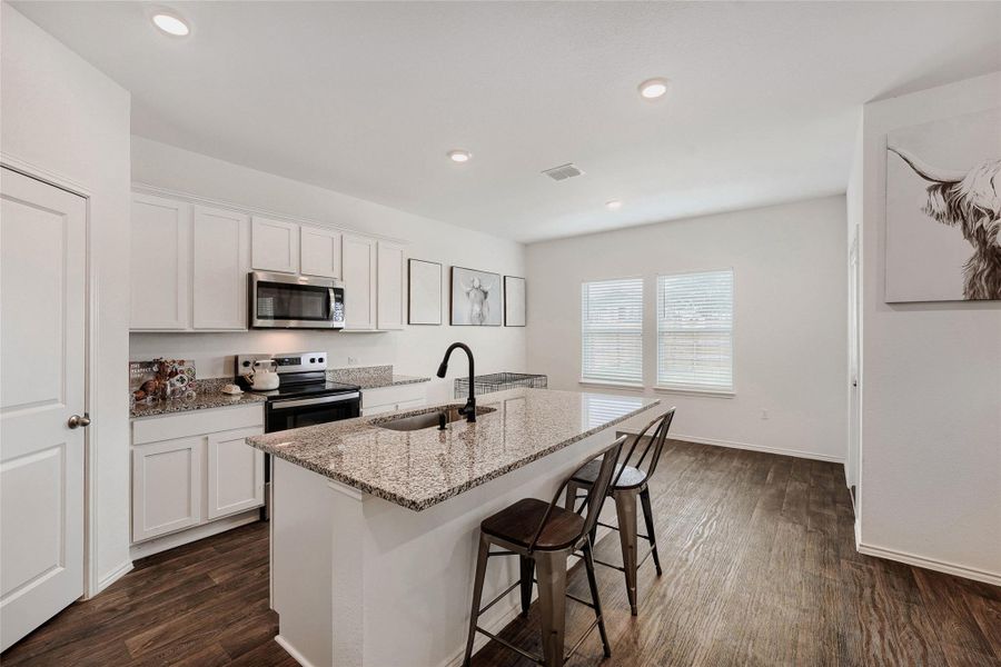 Kitchen featuring a granite-topped island with an integrated sink, wood-finish flooring, white cabinetry, stainless steel appliances, and recessed lighting Kitchen featuring a granite-topped island with an integrated sink, wood-finish flooring, white cabinetry, stainless steel appliances, and recessed lighting