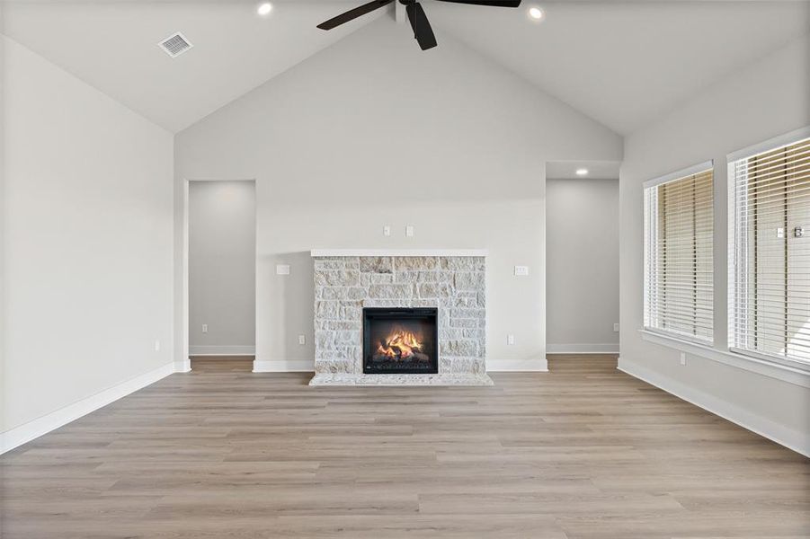 Unfurnished living room featuring light wood-style flooring, a stone fireplace, high vaulted ceiling, recessed lighting, and a ceiling fan