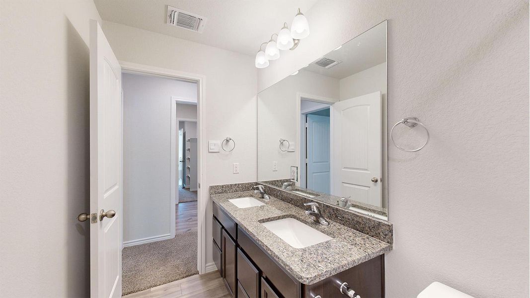 Bathroom vanity featuring dual undermount sinks, a granite countertop, and a large wall-mounted mirror with an overhead light fixture Bathroom vanity featuring dual undermount sinks, a granite countertop, and a large wall-mounted mirror with an overhead light fixture