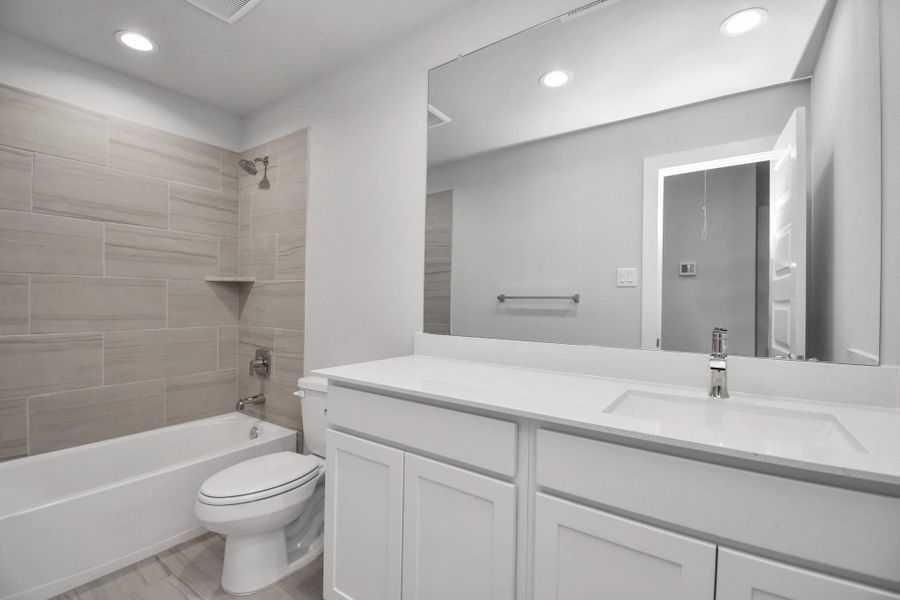 Secondary bath features tile flooring, bath/shower combo with tile surround, light stained wood cabinets, beautiful light countertop.