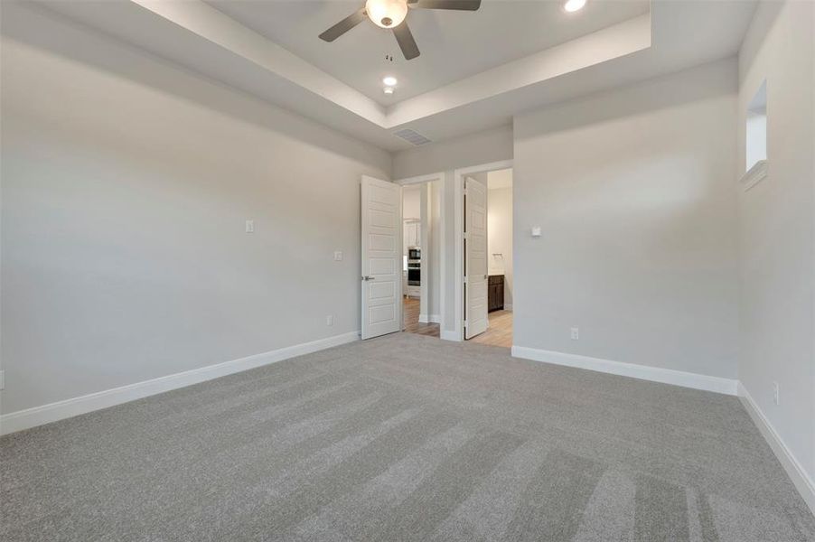 Unfurnished bedroom with light carpet, a raised ceiling, ceiling fan, recessed lighting, and ensuite bath