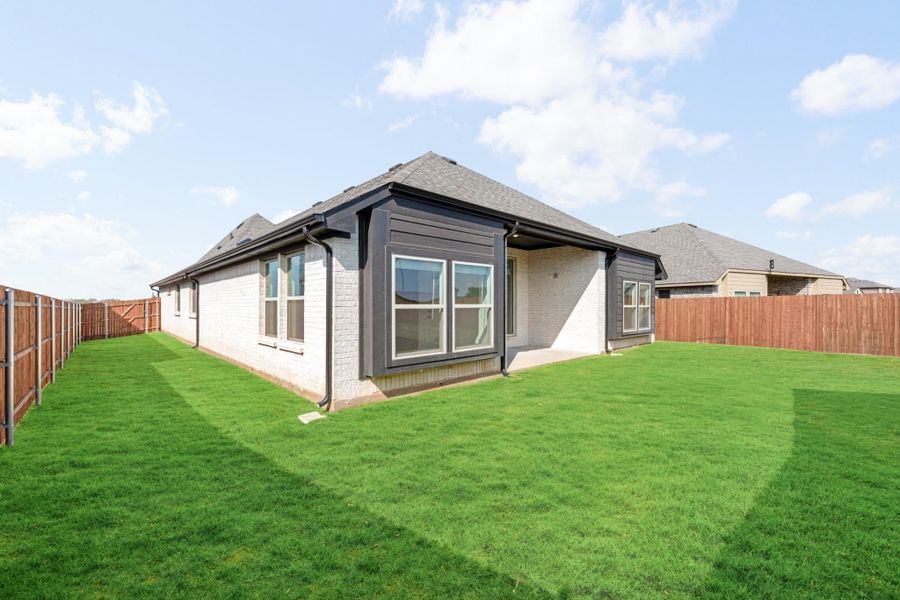 Back of single-story brick home with dark trim, large windows, green lawn, and wood privacy fence.